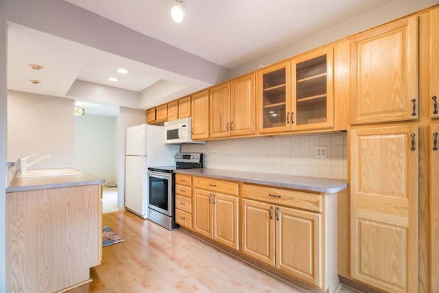 kitchen with a tray ceiling, a sink, white appliances, glass insert cabinets, and light wood-style flooring