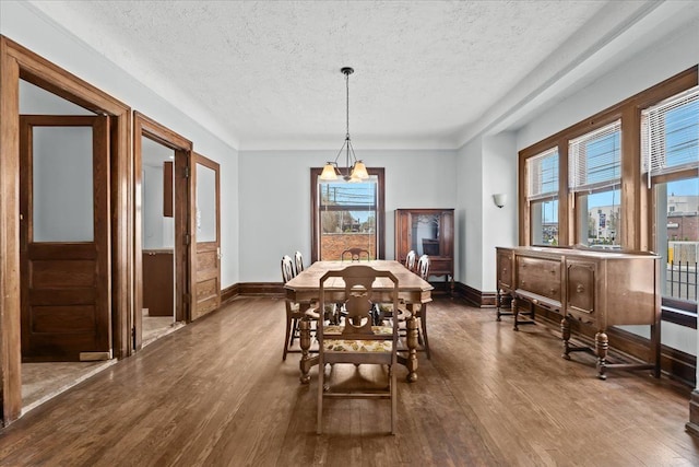 dining space with a textured ceiling, dark wood finished floors, a wainscoted wall, baseboards, and an inviting chandelier
