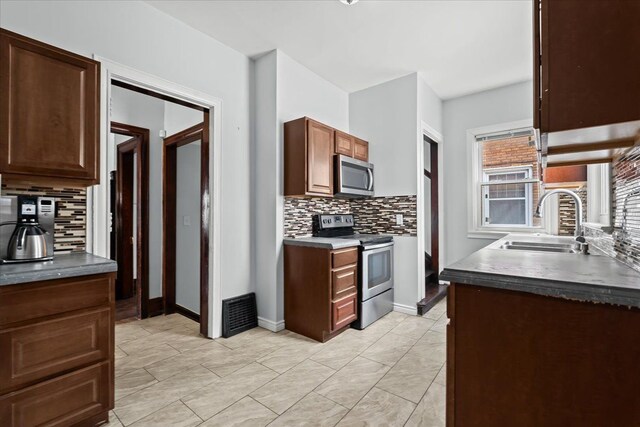 kitchen with dark countertops, a sink, stainless steel appliances, baseboards, and backsplash