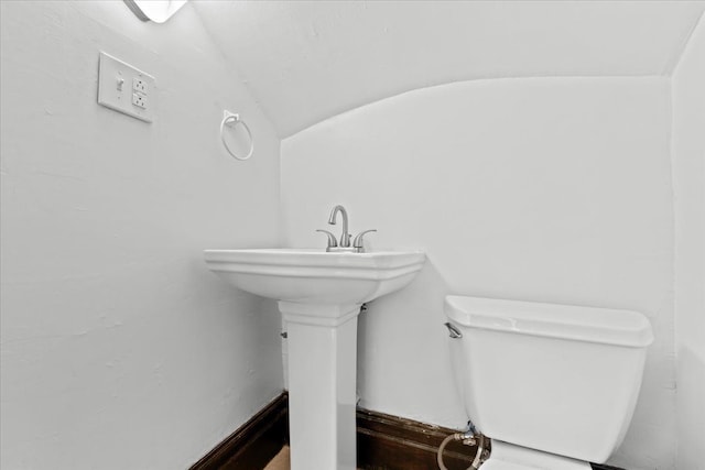 bathroom with toilet, vaulted ceiling, and a sink