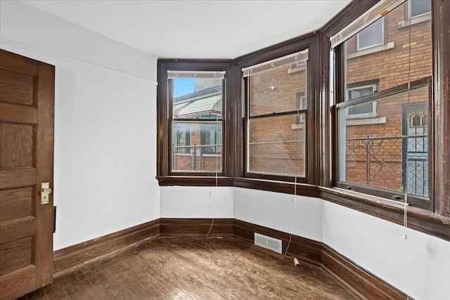 empty room featuring wood-type flooring, baseboards, and visible vents