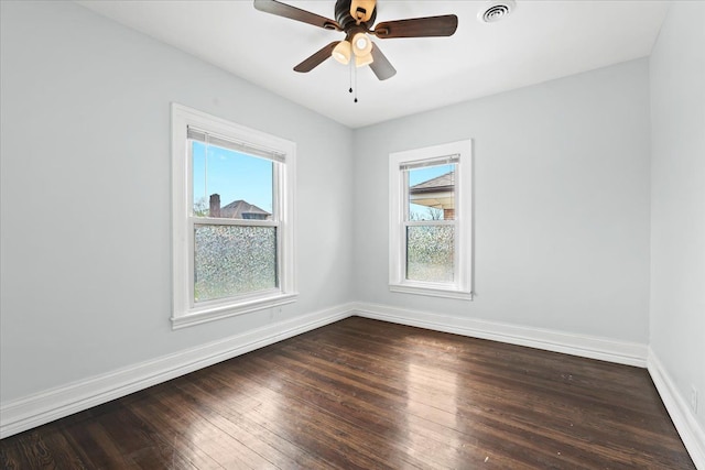 empty room featuring a healthy amount of sunlight, baseboards, dark wood-style flooring, and visible vents