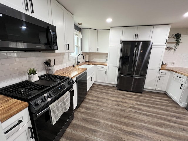 kitchen with wood finished floors, a sink, black appliances, butcher block counters, and backsplash