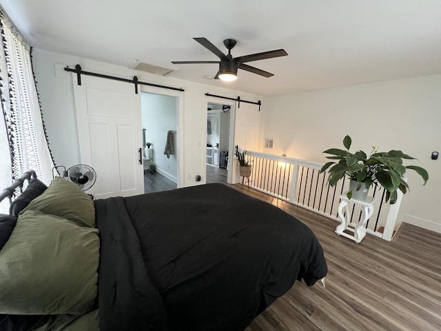 bedroom with visible vents, baseboards, wood finished floors, and a barn door