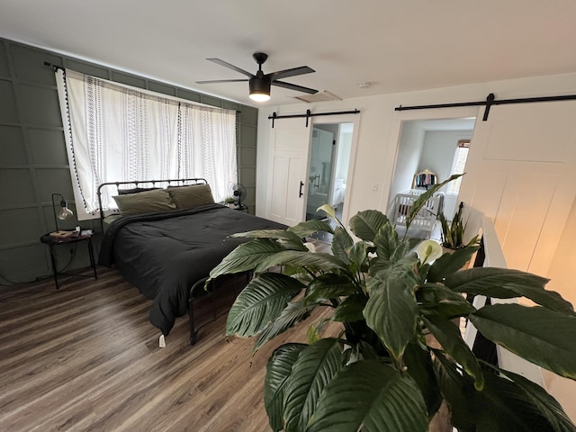 bedroom with a barn door, wood finished floors, ceiling fan, and ensuite bathroom