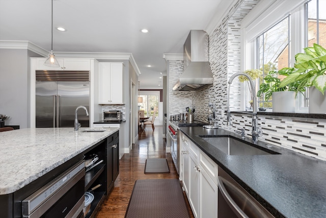 kitchen featuring built in appliances, tasteful backsplash, wall chimney range hood, and a sink