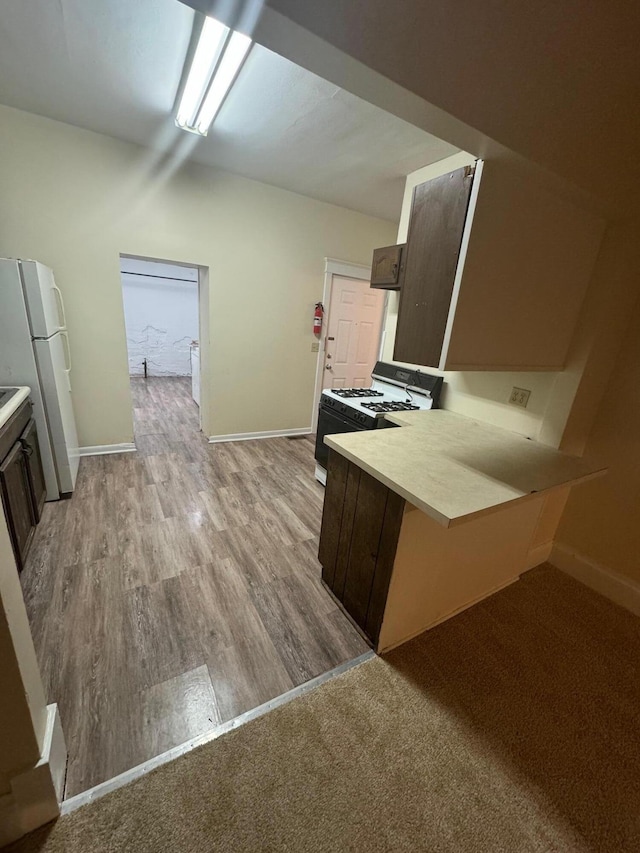 kitchen featuring a peninsula, light countertops, freestanding refrigerator, and range with gas cooktop