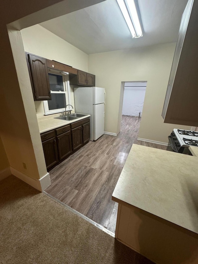 kitchen with dark brown cabinetry, light countertops, freestanding refrigerator, and a sink
