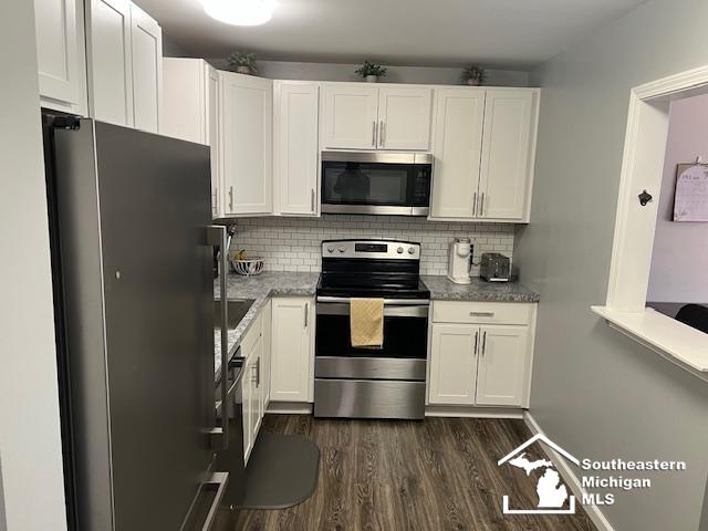 kitchen featuring stainless steel appliances, decorative backsplash, white cabinetry, and dark wood-style flooring