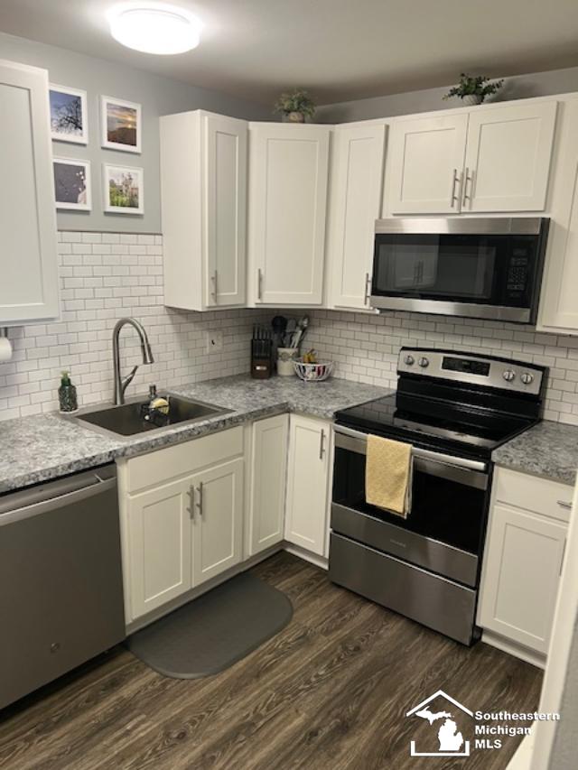 kitchen featuring white cabinets, dark wood-style floors, stainless steel appliances, a sink, and decorative backsplash