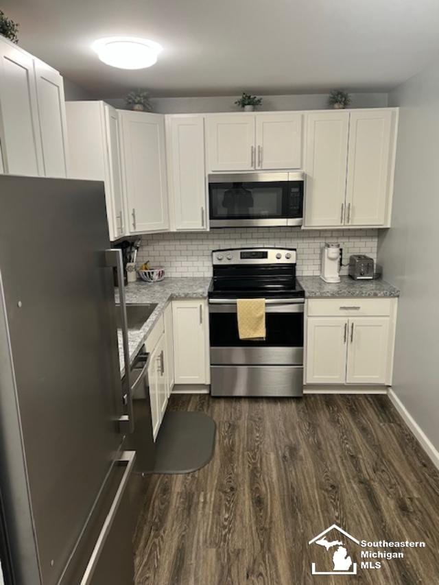 kitchen featuring decorative backsplash, stainless steel appliances, baseboards, white cabinetry, and dark wood-type flooring