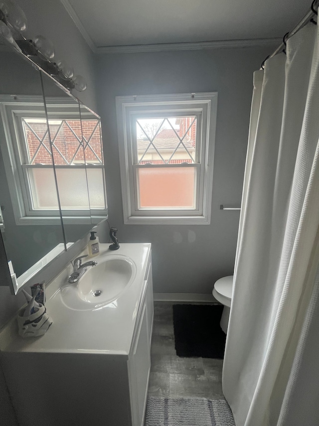 bathroom featuring toilet, baseboards, wood finished floors, crown molding, and vanity