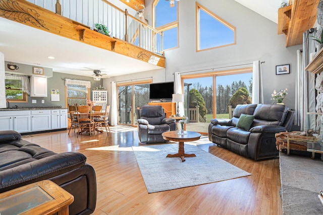 living room with light wood-style flooring, a high ceiling, a ceiling fan, and plenty of natural light