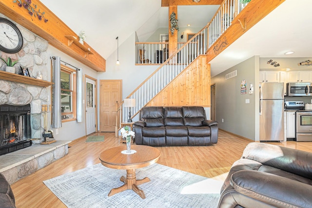 living room featuring light wood finished floors, a stone fireplace, visible vents, stairs, and high vaulted ceiling