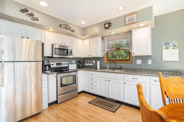 kitchen featuring white cabinetry, light wood-style flooring, stainless steel appliances, and a sink