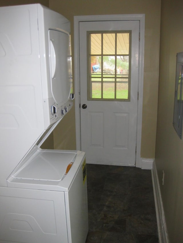 washroom with stacked washer and dryer, electric panel, baseboards, and laundry area