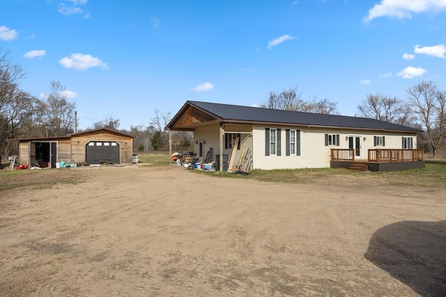 rear view of property featuring dirt driveway, metal roof, an outdoor structure, a detached garage, and a deck