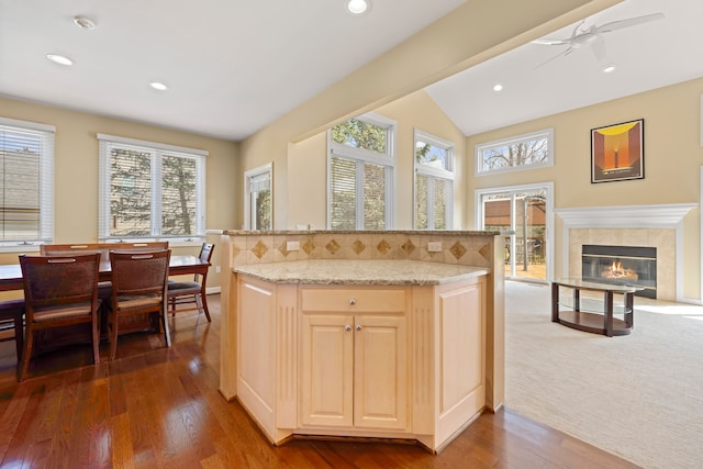kitchen with a fireplace, ceiling fan, light stone counters, vaulted ceiling, and wood finished floors
