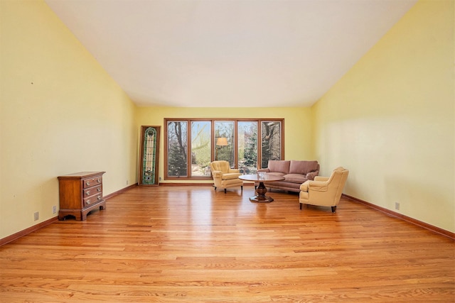 living area featuring light wood-type flooring, lofted ceiling, and baseboards