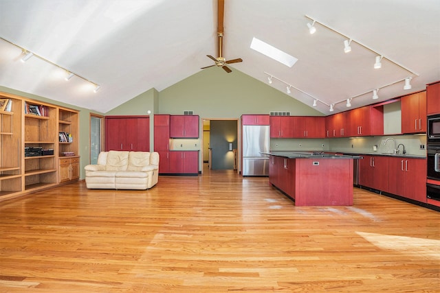 kitchen with light wood-type flooring, dark countertops, a skylight, stainless steel refrigerator, and track lighting
