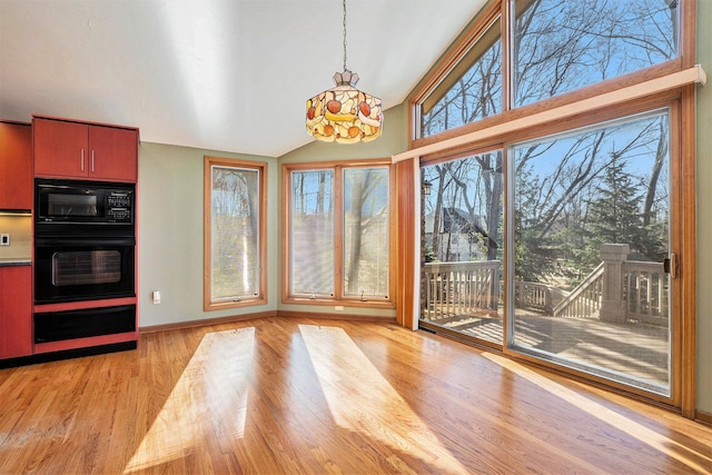 unfurnished dining area featuring light wood-style flooring, baseboards, a wealth of natural light, and vaulted ceiling