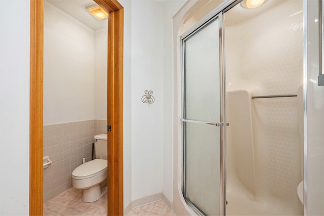 bathroom with a shower stall, toilet, tile patterned flooring, and tile walls