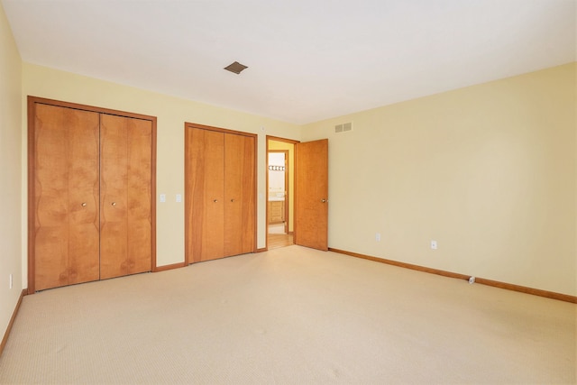 unfurnished bedroom with baseboards, visible vents, two closets, and light colored carpet