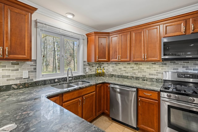 kitchen with a sink, light tile patterned floors, dark stone countertops, ornamental molding, and stainless steel appliances