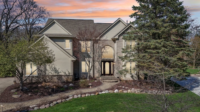 traditional-style home featuring a shingled roof, a front lawn, and brick siding