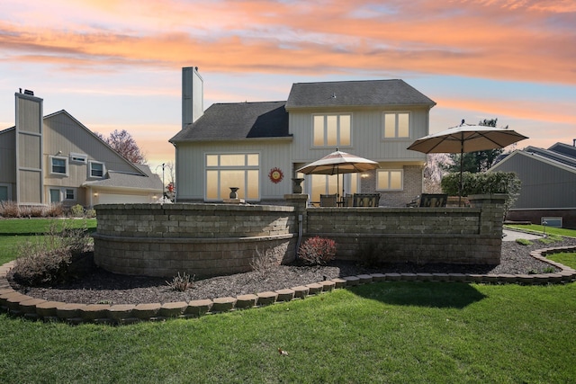 back of property at dusk featuring fence, a chimney, a yard, and brick siding