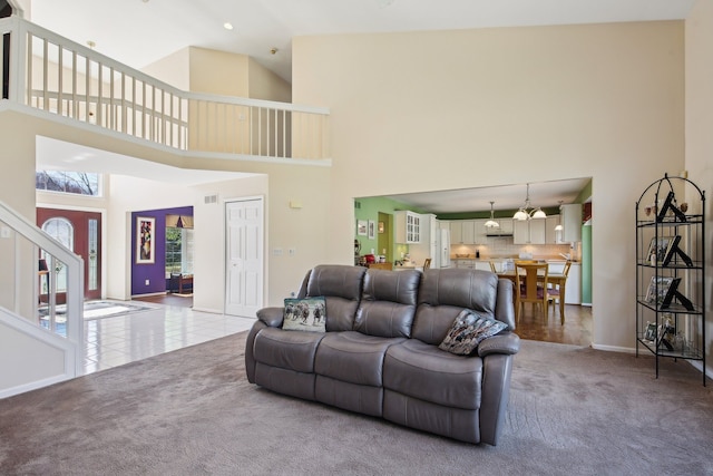 tiled living room with visible vents, a towering ceiling, stairway, carpet floors, and baseboards