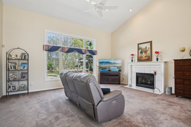 carpeted living room with plenty of natural light, ceiling fan, a tiled fireplace, and high vaulted ceiling