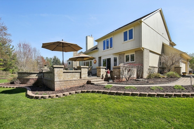 rear view of house featuring a chimney, a yard, and brick siding