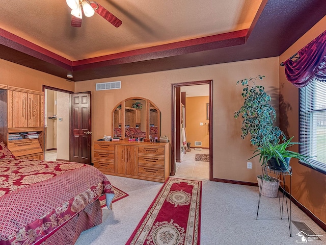 bedroom with visible vents, connected bathroom, a raised ceiling, and light colored carpet