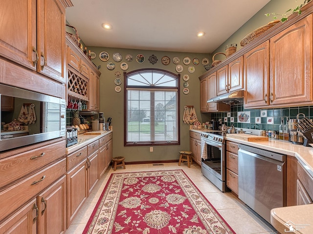 kitchen with light countertops, under cabinet range hood, appliances with stainless steel finishes, and decorative backsplash