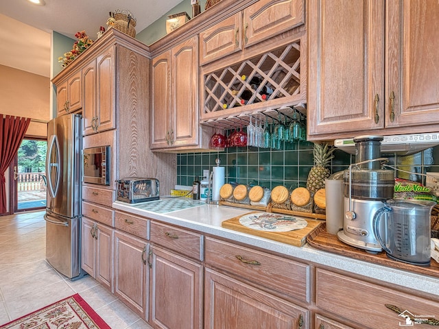 kitchen with light countertops, light tile patterned flooring, decorative backsplash, brown cabinetry, and appliances with stainless steel finishes