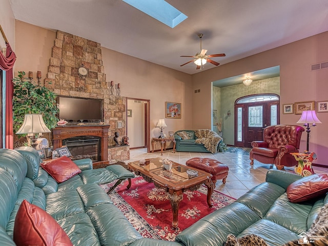tiled living area featuring a fireplace, visible vents, a ceiling fan, and a skylight