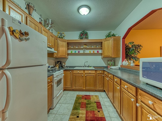 kitchen featuring dark countertops, a sink, under cabinet range hood, and white appliances