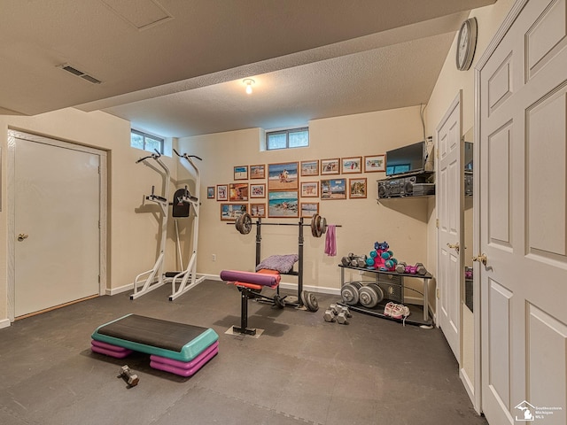workout room featuring baseboards, a textured ceiling, and visible vents
