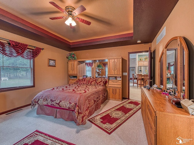 bedroom with visible vents, a textured ceiling, light colored carpet, and a tray ceiling