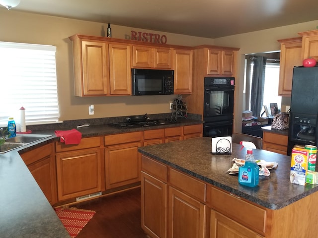 kitchen with black appliances, a wealth of natural light, a center island, and dark wood-type flooring