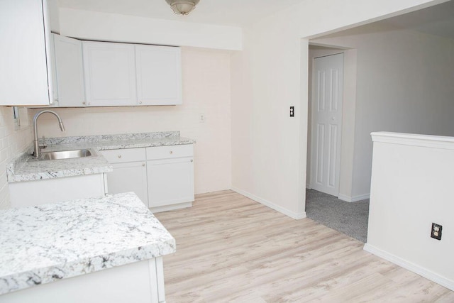kitchen with light countertops, a sink, light wood-style floors, baseboards, and white cabinetry