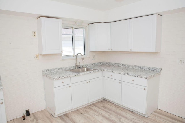 kitchen with light wood finished floors, light stone countertops, white cabinets, and a sink