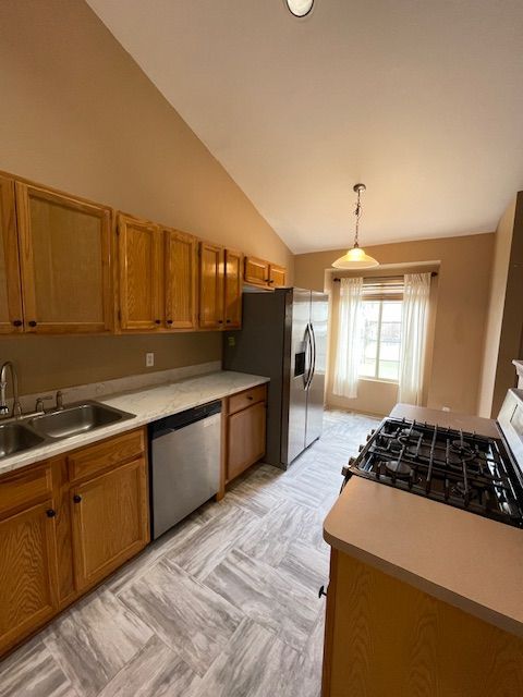 kitchen with brown cabinetry, lofted ceiling, appliances with stainless steel finishes, and a sink