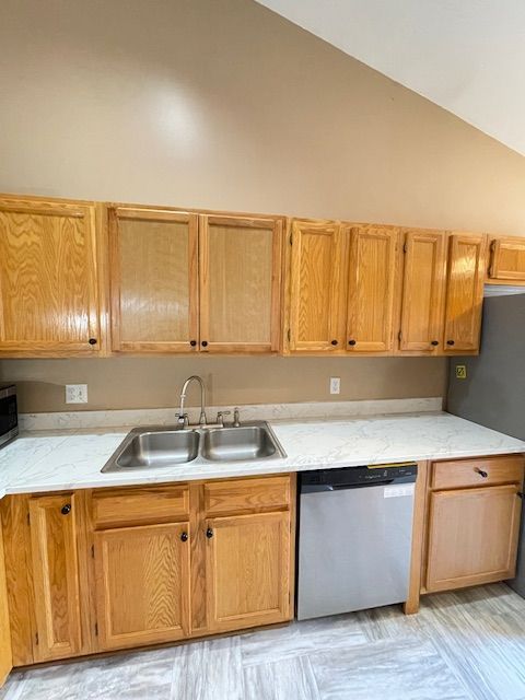 kitchen featuring dishwasher, light stone counters, a sink, and high vaulted ceiling