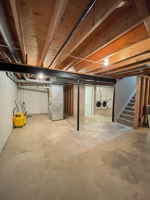 unfinished below grade area featuring stairway, heating unit, and separate washer and dryer
