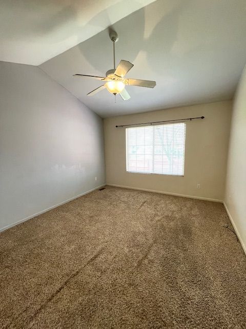 carpeted spare room featuring vaulted ceiling, baseboards, and a ceiling fan