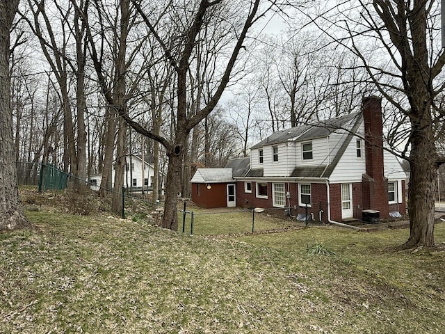 exterior space with a front lawn, central air condition unit, a chimney, fence, and brick siding