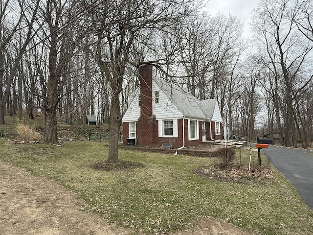 view of side of home featuring a chimney, brick siding, and a yard