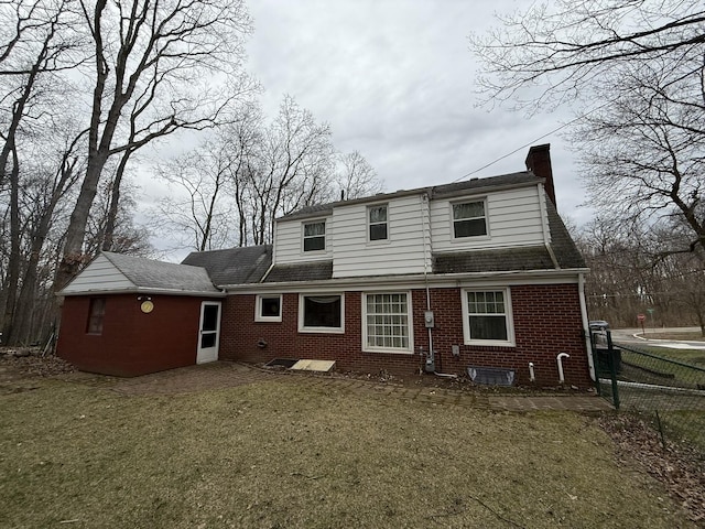 rear view of property featuring a lawn, brick siding, fence, and a chimney